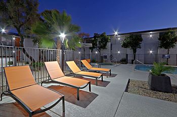 an outdoor patio with orange lounge chairs and a pool at night at Allora Phoenix in Arizona 85021